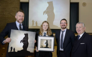 Four people posing for the picture, with one of them holding a prize after naming a sculptured bear.