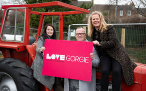 Lynn Bell, Garry Hutton and Kim Flower sitting on a tractor and holing up a LOVE Gorgie Farm banner