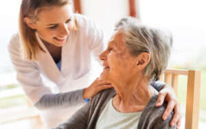 A carer and an elderly woman smile at each other.